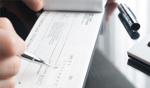 Hand writing a check with pen on a checkbook, on a metal desk surface